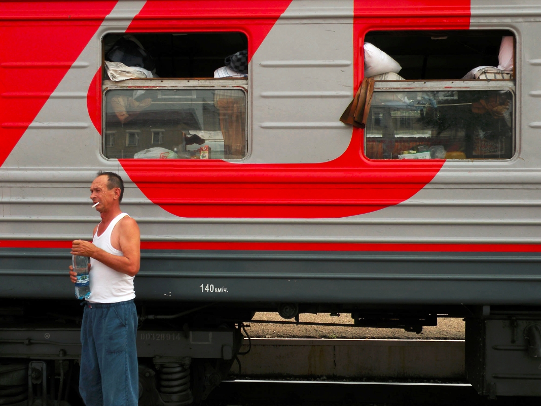 A man stands in front of a sleeper car. Some are divided into four-bed compartments, others are more communal with beds arranged around an open center isle.