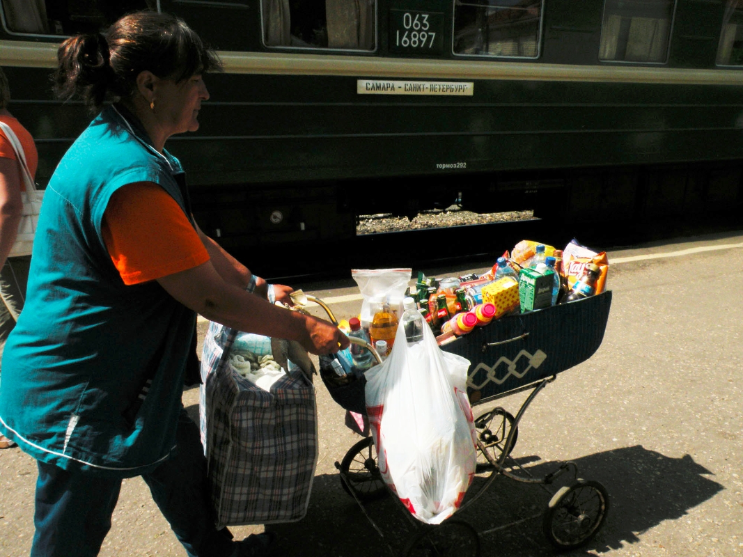 A woman sells snacks on a platform. It is typical to see local vendors with home-made treats (and contraptions to hold them) on a railway journey.